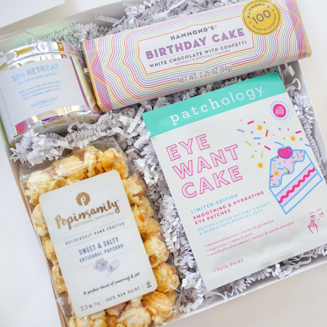 Gift box with popcorn, chocolate bar, and eye mask on a white background