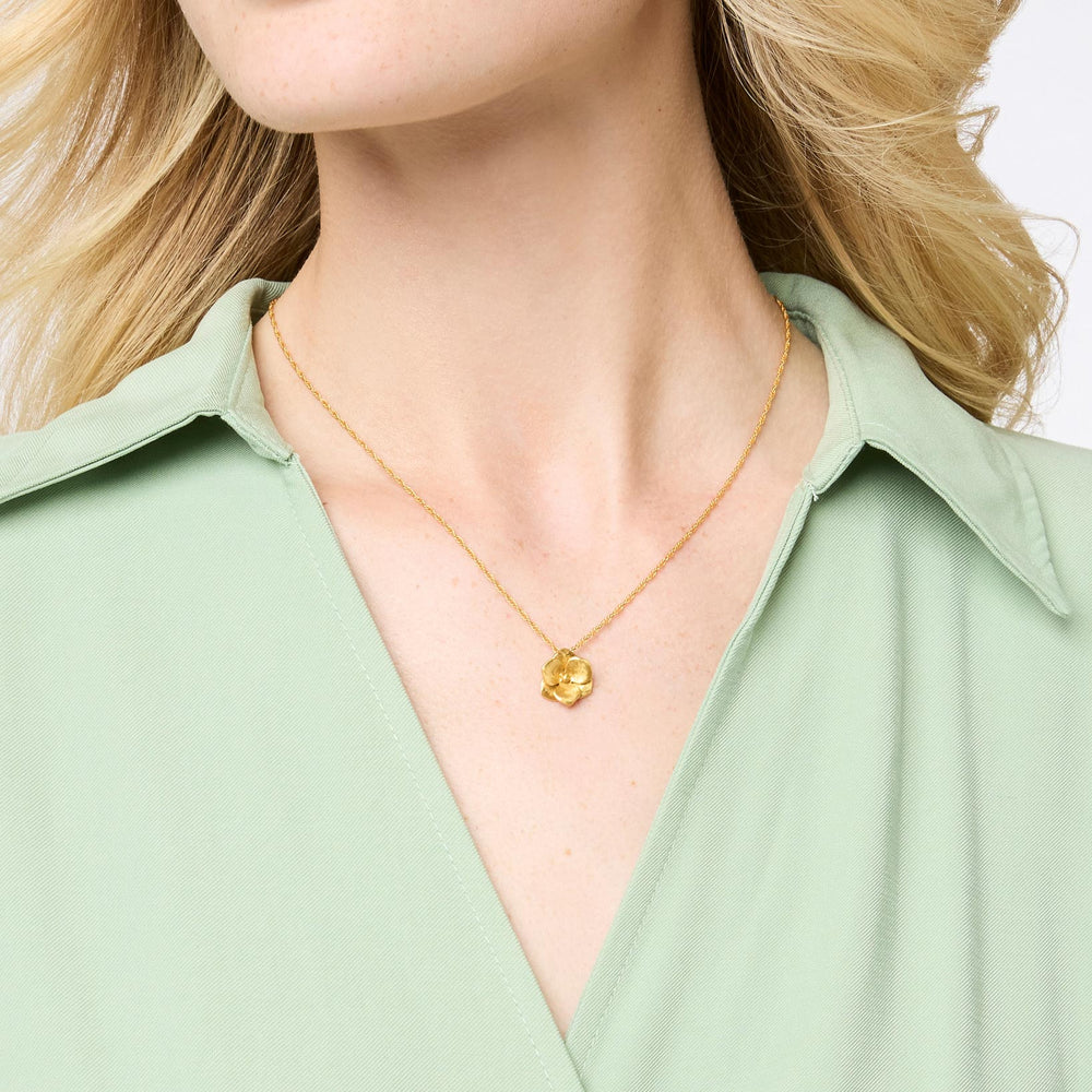 Photograph of a Michael Michaud gold hydrangea necklace worn on a woman's neck featuring a matte-finished floral pendant, a delicate gold chain, and a light sage green collared shirt