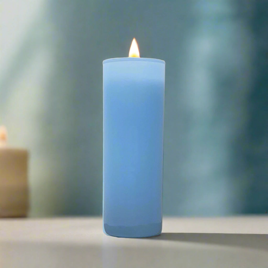 Digital photograph of a burning light blue pillar candle on a neutral tabletop featuring a bright flickering flame and a soft teal bokeh background