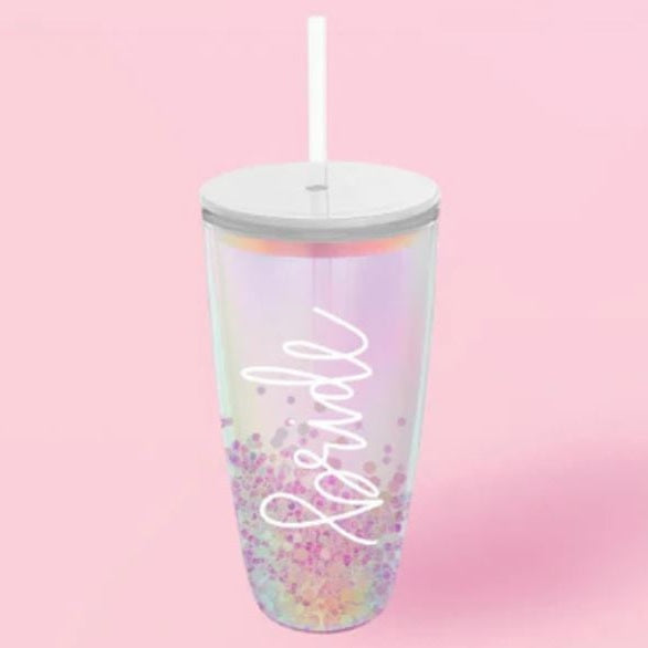 Product photograph of an iridescent bridal tumbler set against a pink background featuring white cursive script, a white lid and straw, and pastel purple confetti at the base