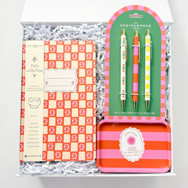 Stationery set with checkered notebook, colorful pencils, and a striped tin in a box on a white background