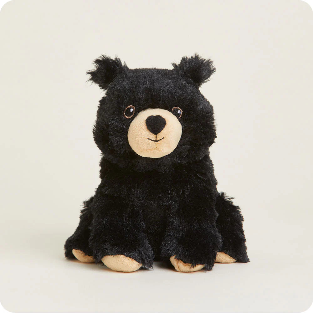 Plush toy of a black bear cub sitting in a studio setting with fluffy black fur, a cream-colored muzzle, and small brown eyes