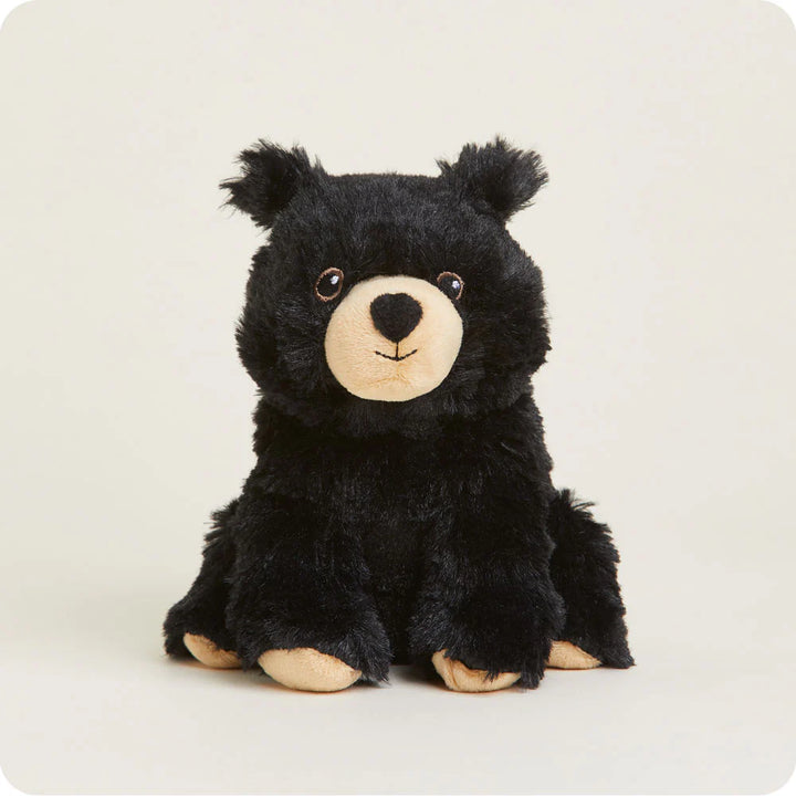 Plush toy of a black bear cub sitting in a studio setting with fluffy black fur, a cream-colored muzzle, and small brown eyes