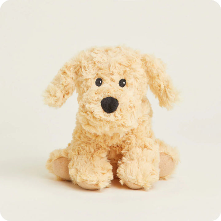 Plush toy by Jellycat of a sitting cream labradoodle puppy on a neutral background featuring shaggy textured fur, a prominent black embroidered nose, and beige suede-like paw pads