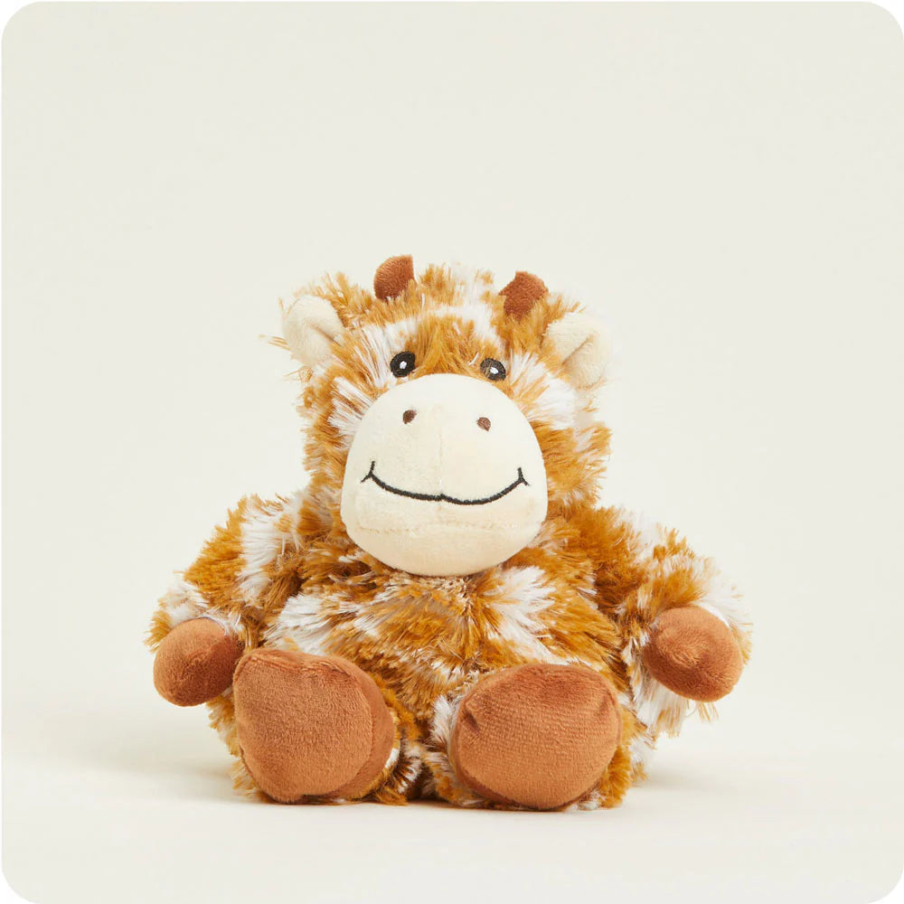 Plush stuffed toy by Warmies of a sitting giraffe on an off-white background featuring mottled orange-brown and white faux fur, a cream-colored muzzle with a stitched black smile, and small brown ossicones