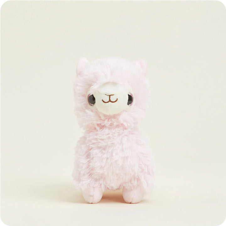 Plush toy of a soft pink alpaca against a neutral studio backdrop featuring its characteristic fluffy pastel fur, large shiny black eyes, and a small white muzzle with an embroidered brown smile