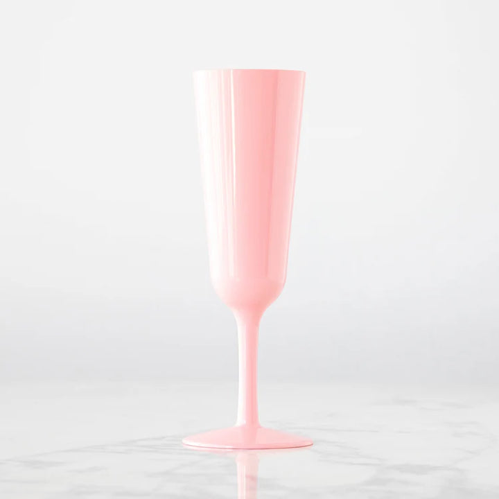 Opaque pink plastic champagne flute standing on a white marble surface featuring a slender tapered stem and a soft pastel finish against a minimalist white background