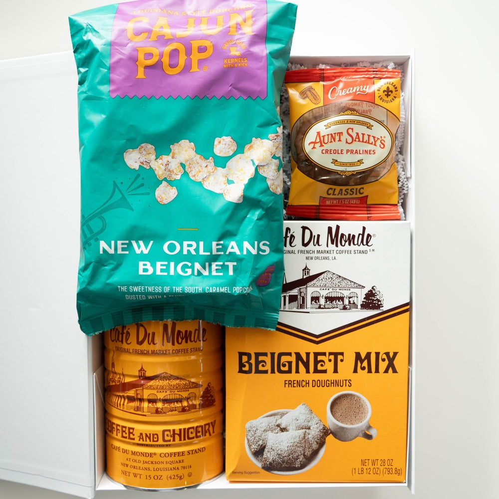 Photograph of a New Orleans snack gift set featuring a vibrant teal bag of beignet popcorn and Café Du Monde coffee products displaying the iconic French Market landmark and powdered sugar-dusted beignets