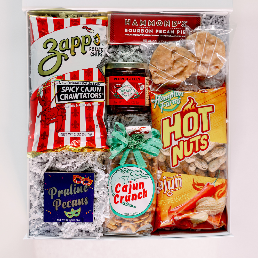 A photograph of a New Orleans themed snack gift box featuring Zapp’s Spicy Cajun Crawtators and Tabasco Pepper Jelly nestled in white shredded paper with a bright teal ribbon and colorful Mardi Gras mask illustrations
