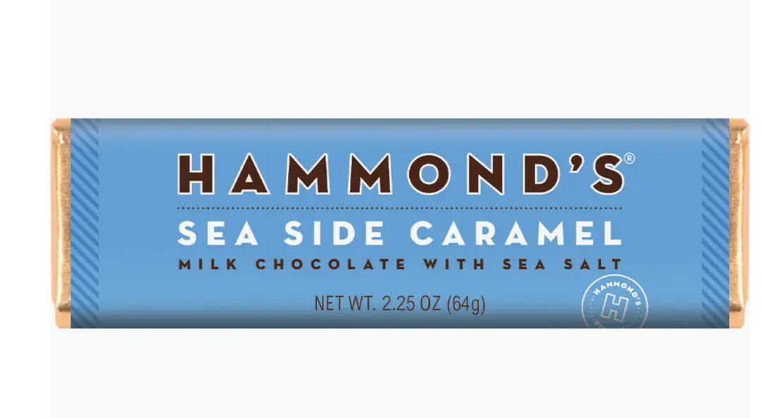 Graphic design packaging by Hammond's Candies of a Sea Side Caramel milk chocolate bar centered on a white background featuring a light blue wrapper, gold foil ends, and the iconic brand logo in bold brown lettering