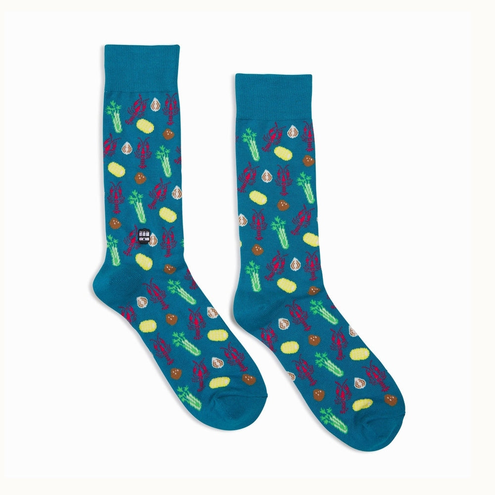 Patterned knit socks by Bonfolk featuring a New Orleans crawfish boil theme with iconic St. Charles streetcars, vibrant red crawfish, and bright yellow corn cobs on a teal background
