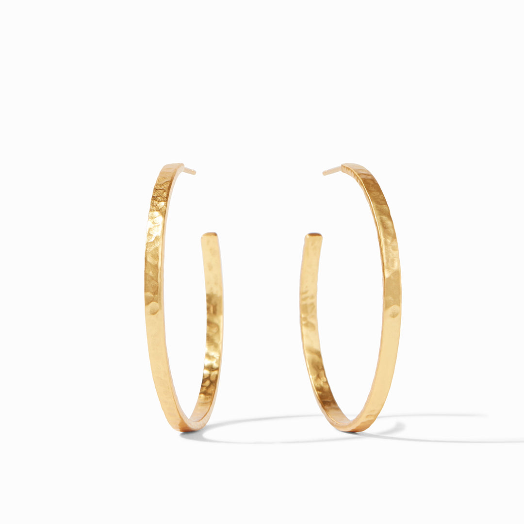 Hammered gold jewelry by Julie Vos featuring a pair of large open hoop earrings on a minimalist white background with a glistening dimpled texture and a warm light-reflecting finish