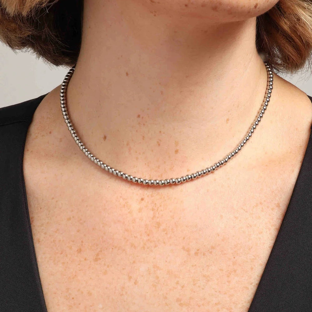 Digital photograph of a silver beaded necklace worn on a woman's neck featuring small polished spherical links and freckled skin against a black V-neck top