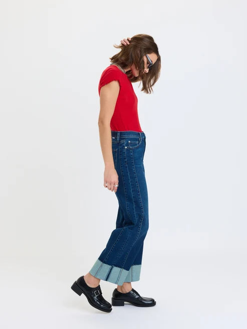 Studio photograph of a woman model in a white studio wearing a vibrant red short-sleeved top and dark blue denim jeans featuring wide light blue cuffed hems paired with black platform loafers with silver buckles