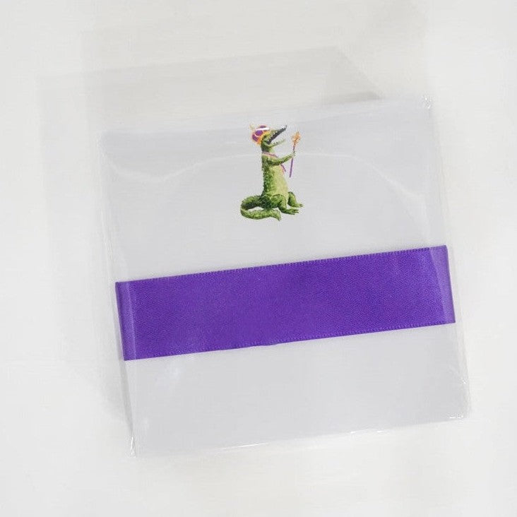 Watercolor illustration stationery set featuring a New Orleans Mardi Gras alligator wearing a purple and gold crown and holding a scepter, wrapped in a wide purple satin ribbon