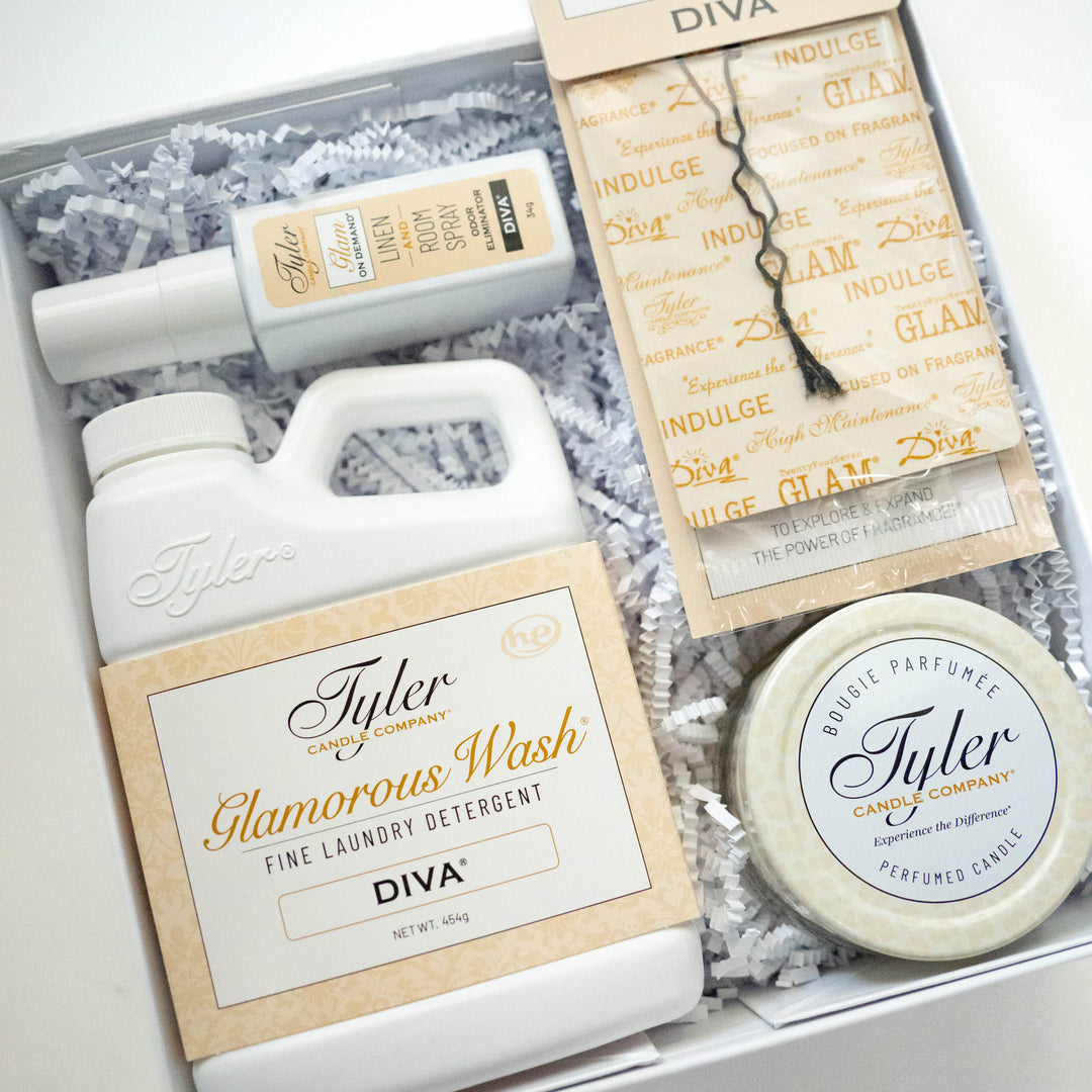 Photograph of a Tyler Candle Company Diva gift box containing Glamorous Wash laundry detergent and a perfumed candle nestled in white crinkle paper with elegant gold script labels and a sachet tied with a black string