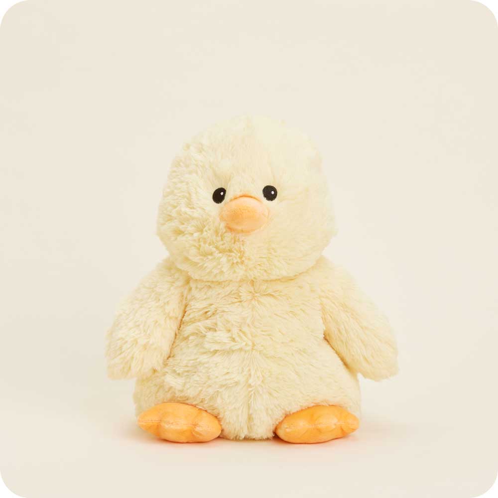 Photograph of a Jellycat Nivell Chick plush toy on a plain off-white background featuring soft cream-colored textured fur, a small smooth orange beak, and bright orange webbed feet
