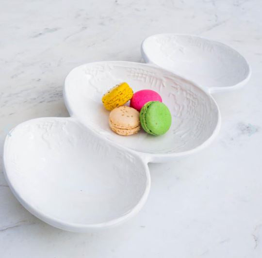 White ceramic triple-sectioned serving dish featuring embossed Willow pattern pagoda and bridge scenes on a marble surface holding vibrant yellow, neon pink, and lime green macarons