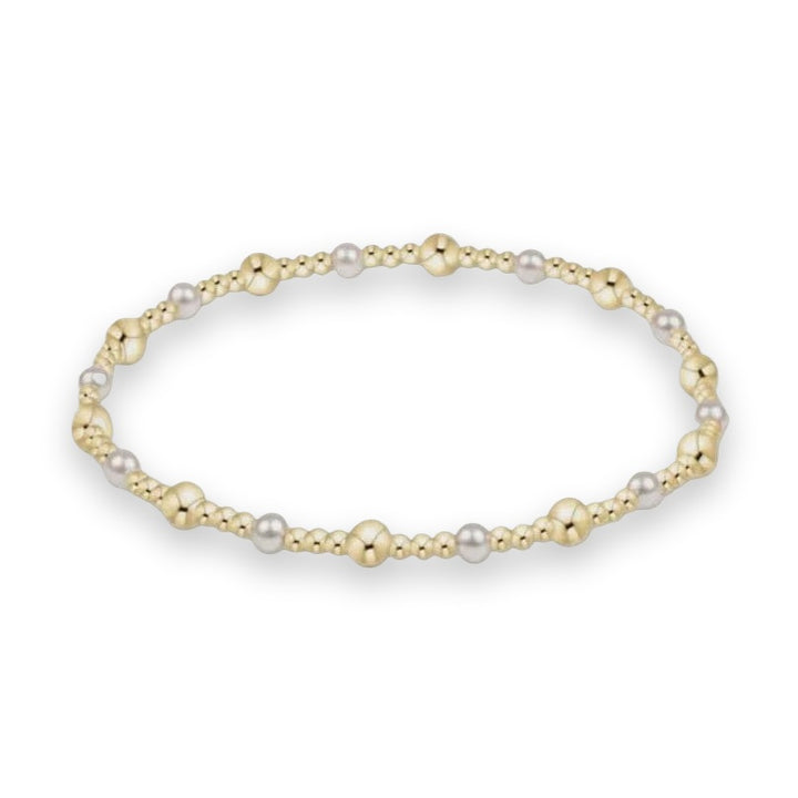 Gold and silver beaded bracelet centered on a light gray background featuring polished metallic spheres of varying sizes in a rhythmic alternating pattern