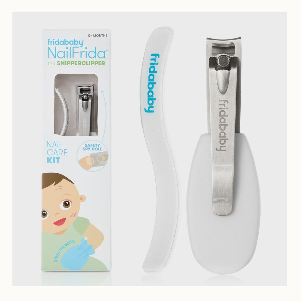 Product photography for Fridababy showcasing the NailFrida SnipperClipper kit against a neutral background, featuring a stainless steel clipper with a safety spy hole, an s-curved white nail file with teal branding, and a colorful retail box with a cartoon infant illustration