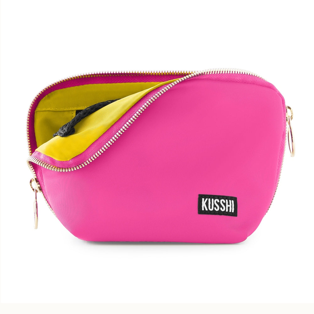 Product photography of a Kusshi makeup bag featuring a vibrant hot pink exterior, a contrasting bright yellow interior lining, and gold-toned zippers with a black and white brand label against a white background