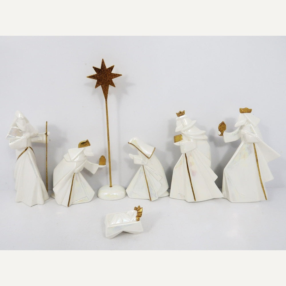 Ceramic porcelain nativity scene depicting the Three Wise Men, Mary, Joseph, and Baby Jesus beneath a tall golden Star of Bethlehem on a white background, characterized by faceted geometric silhouettes, an iridescent pearl finish, and elegant gold-trimmed edges