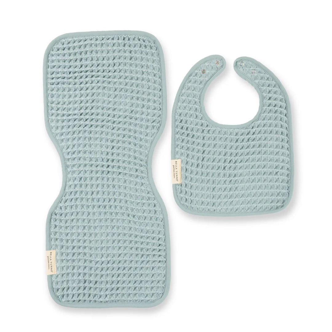 Waffle knit fabric by Bella Tunno featuring a pale eucalyptus blue baby bib and matching contoured burp cloth set on a white background with prominent brand tags and a textured honeycomb weave