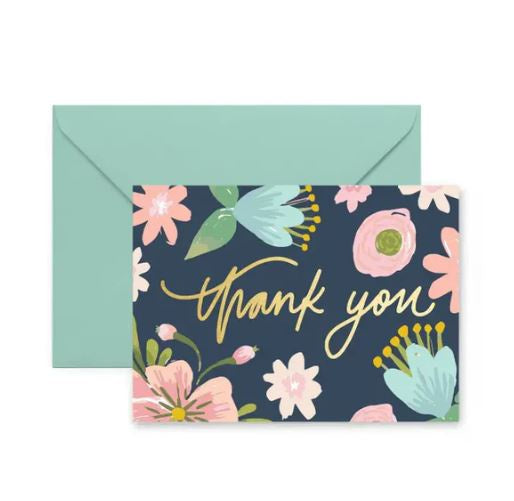 Stationery illustration by Rifle Paper Co featuring a navy blue greeting card with elegant gold foil thank you script and hand-painted pastel pink and blue floral patterns alongside a mint green envelope
