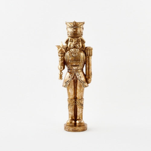 Gilded resin sculpture of a traditional nutcracker soldier centered on a white background featuring a distressed antique gold finish, an ornate crown, and a star-topped scepter