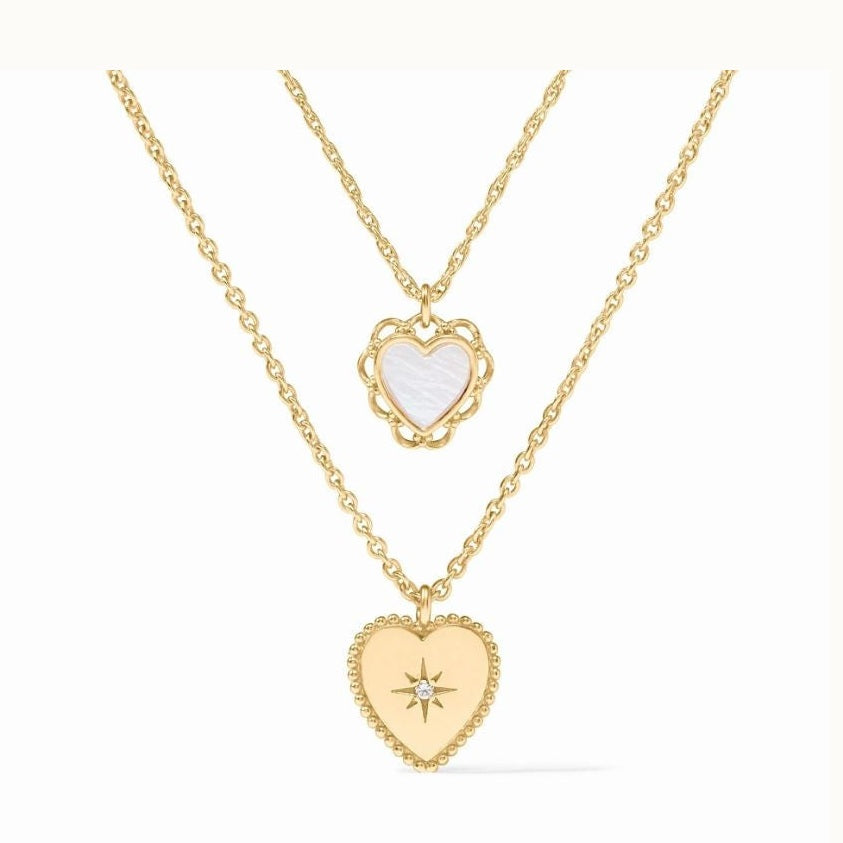 Jewelry photography of two layered gold necklaces centered on a white background featuring iconic heart-shaped pendants, a white mother-of-pearl inlay in a scalloped frame, and a central starburst engraving set with a diamond within a beaded border