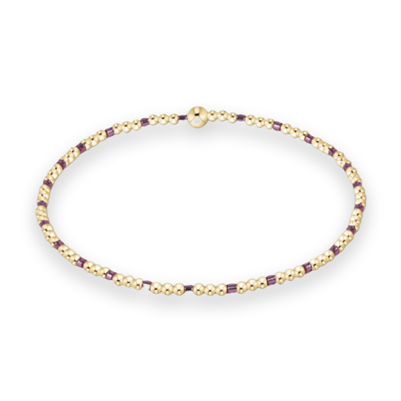 Gold and glass beaded jewelry featuring a delicate circular bracelet of polished gold spheres and small plum-colored cubic accents on a plain white background with a single larger gold bead as a central focal point