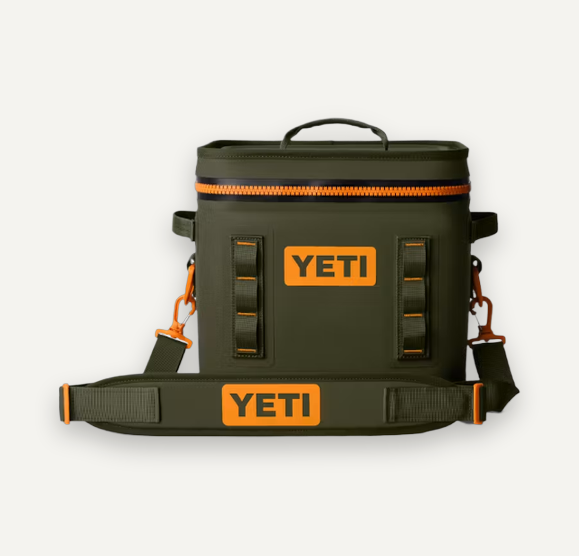 An olive green YETI cooler bag with bright orange accents, including a zipper trim, hardware, and signature orange YETI logos on the front and on the detachable shoulder strap, shown against a light gray background.