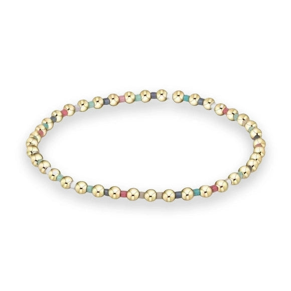 Handcrafted beaded jewelry featuring a dainty gold bracelet on a plain white background showcasing small polished gold spheres and colorful matte teal, pink, and grey cylindrical beads