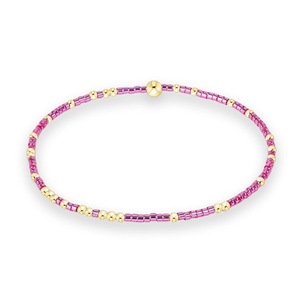 Handcrafted beaded bracelet centered on a white background featuring a large polished gold sphere focal point flanked by alternating metallic pink cylindrical beads and small round gold accents