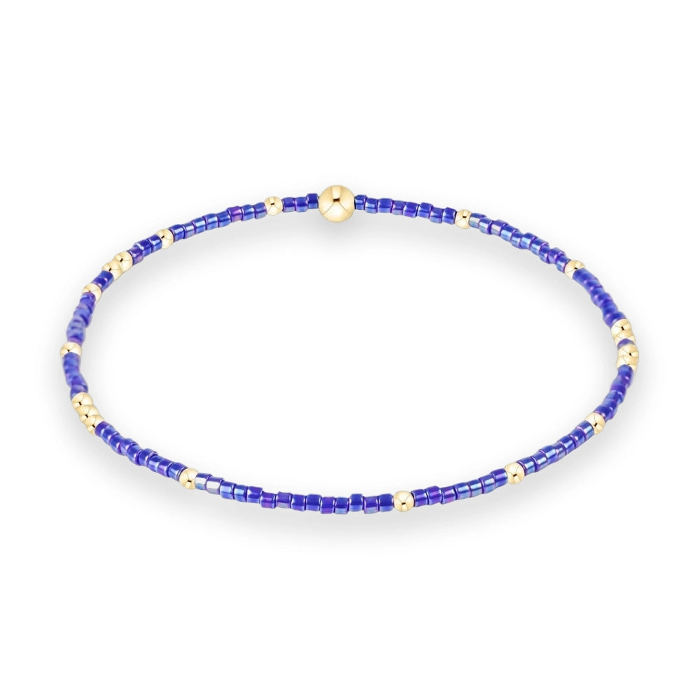 Beaded jewelry featuring a circular bracelet composed of iridescent purple seed beads and polished gold spheres on a white background including a large central gold focal bead and shimmering violet textures