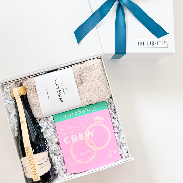 Gift basket with a bottle of champagne, bath bombs, and a card on a white background