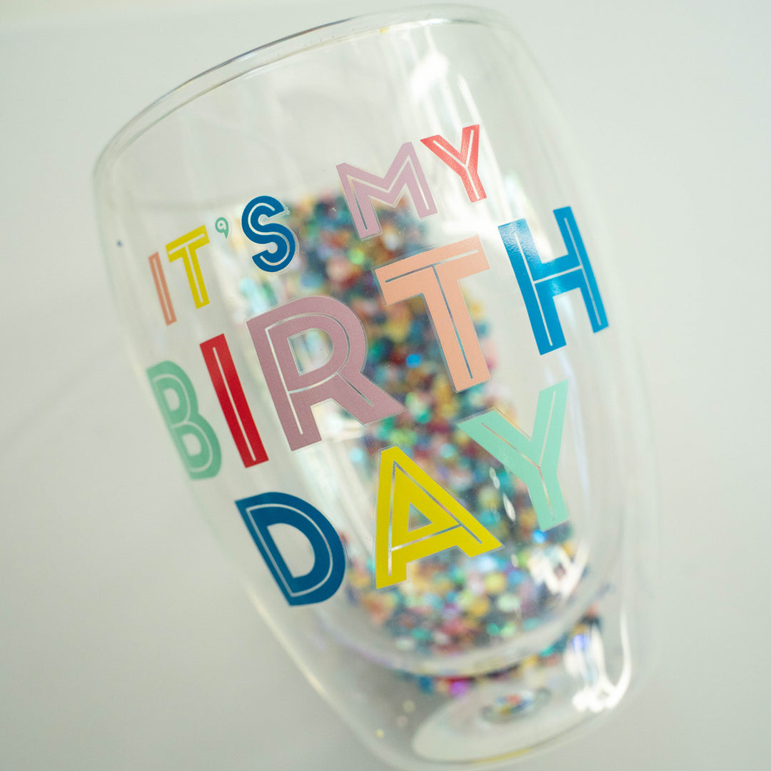 Close-up photograph of a clear glass tumbler featuring the phrase IT&