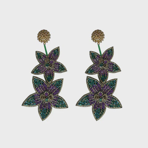 Handcrafted beaded jewelry earrings featuring two tiered star-shaped flowers with vibrant purple and teal seed beads suspended from textured gold circular studs on a neutral white background