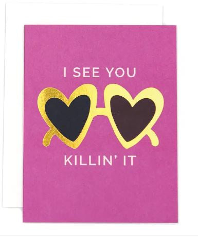 Graphic design greeting card featuring heart-shaped sunglasses with shimmering gold foil frames and dark lenses positioned between white block letters reading I SEE YOU KILLIN' IT on a hot pink background