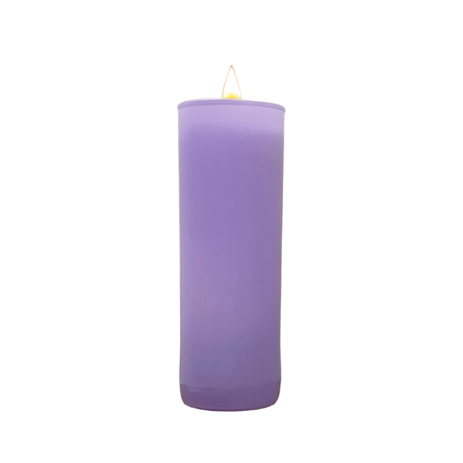 Studio photograph of a tall lavender purple pillar candle in a glass jar centered on a white background featuring a smooth matte texture and a small glowing yellow flame