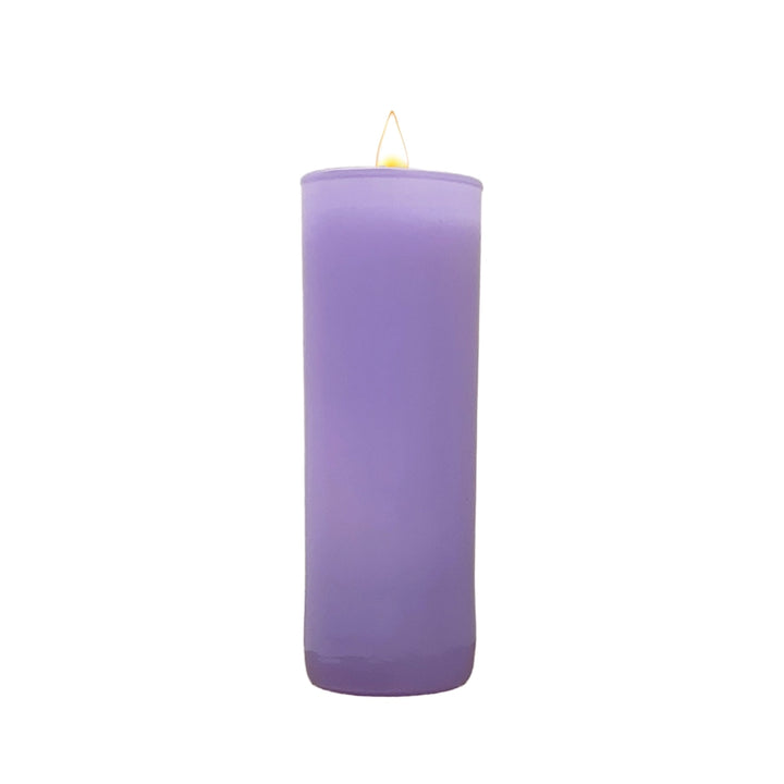 Studio photograph of a tall lavender purple pillar candle in a glass jar centered on a white background featuring a smooth matte texture and a small glowing yellow flame