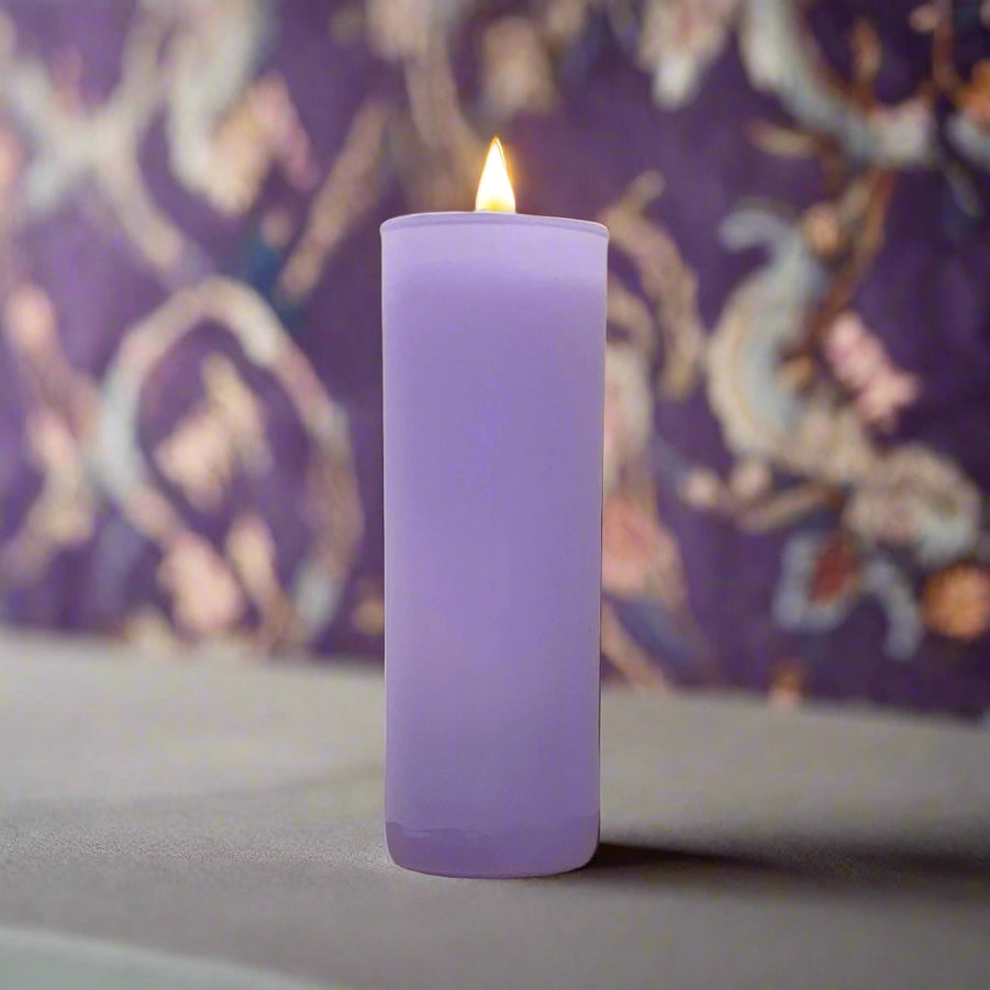 Photograph of a tall lit purple pillar candle on a flat neutral surface featuring a small glowing yellow flame and a blurred violet floral patterned backdrop