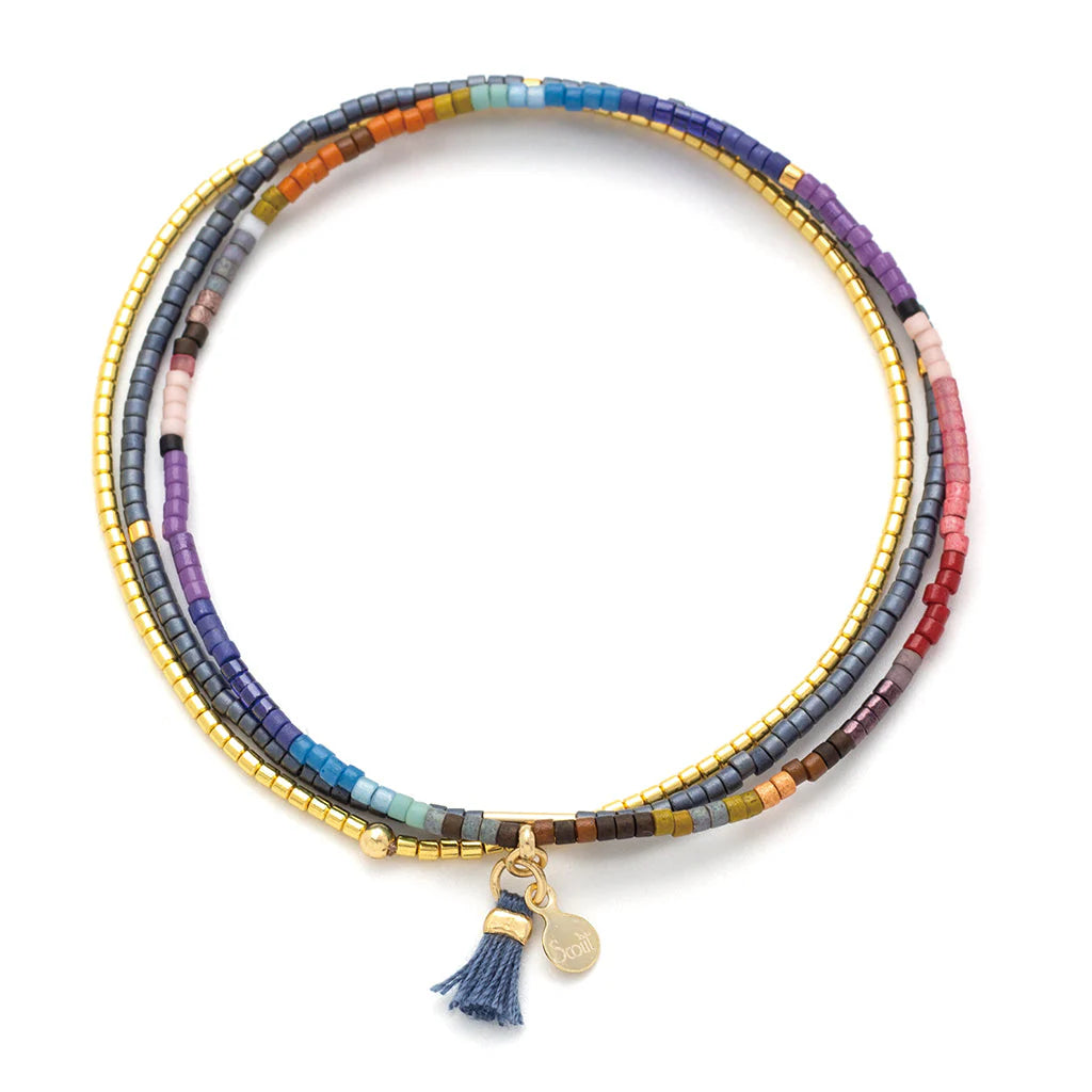 Beaded jewelry by Scout Curated Wear showcases a multi-strand wrap bracelet on a white background featuring a colorful array of matte glass beads, metallic gold accents, and a small blue tassel with a signature gold logo charm