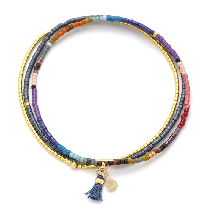 Beaded jewelry by Scout Curated Wear showcases a multi-strand wrap bracelet on a white background featuring a colorful array of matte glass beads, metallic gold accents, and a small blue tassel with a signature gold logo charm