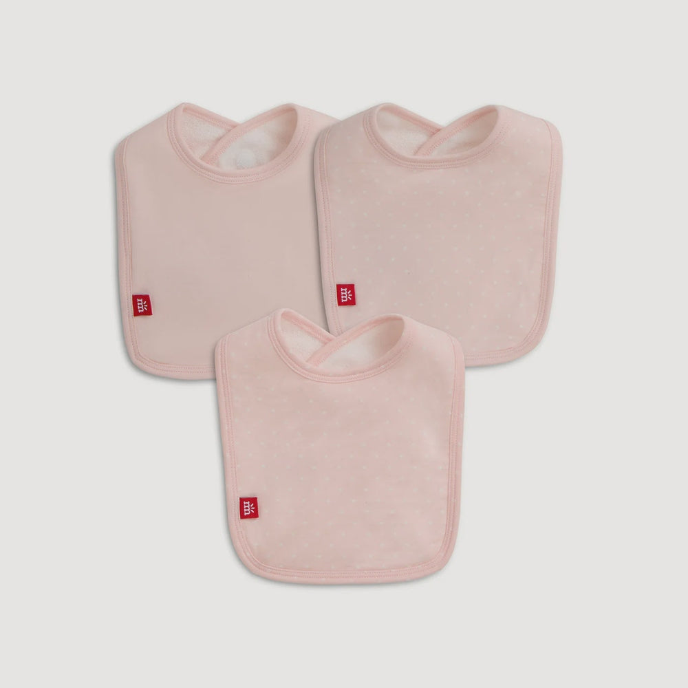 Product photography by Mothercare of three soft pink baby bibs on a neutral grey background featuring subtle white polka dots and signature red logo tags