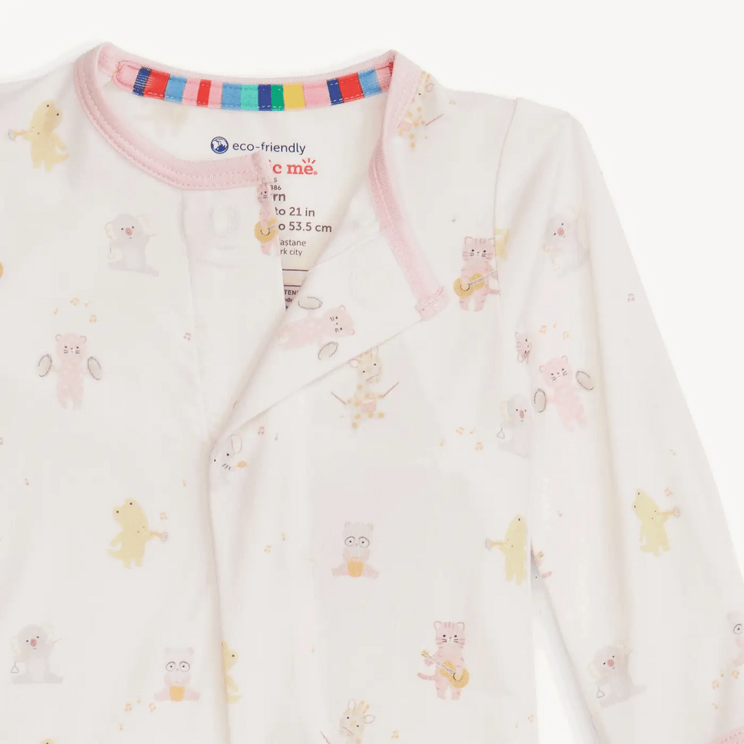 Product photography by Magnetic Me of a white baby onesie featuring a whimsical print of musical animals like cats with guitars and giraffes with drums, accented by a pink neckline and a vibrant rainbow-striped inner collar band