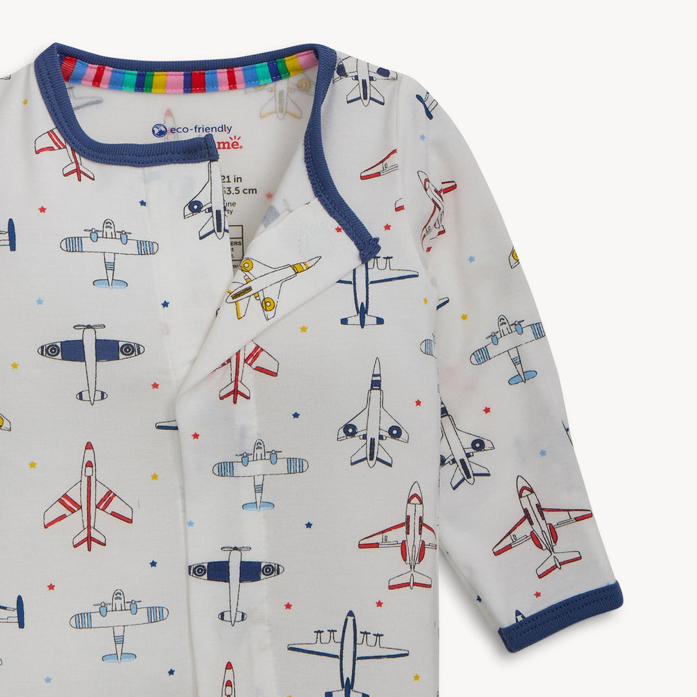 Printed cotton baby onesie by eco-friendly me featuring an all-over airplane pattern on a white background with navy blue ribbed trim, a colorful rainbow striped inner collar, and various red and blue illustrated planes with scattered stars