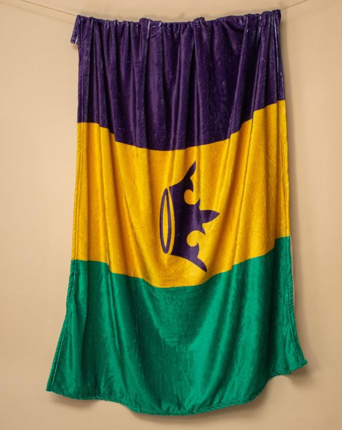 Plush velvet throw blanket featuring the iconic Mardi Gras tricolor bands of purple, gold, and green with a centered purple crown silhouette hanging against a neutral beige background