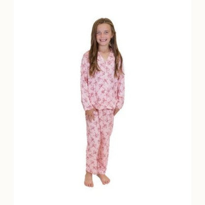 Studio photograph of a smiling young girl with long brown hair wearing a pink pajama set featuring a dark pink floral pattern against a solid white background