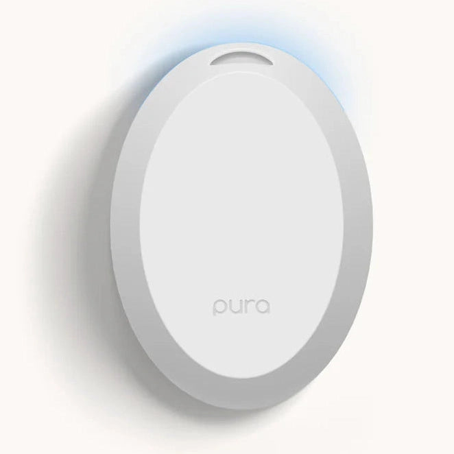 Product photograph by Pura featuring a minimalist white oval smart fragrance diffuser mounted on a wall with a subtle blue LED glow and a small gray logo at the bottom